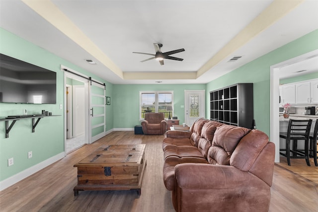 living room featuring ceiling fan, a barn door, light hardwood / wood-style floors, and a tray ceiling