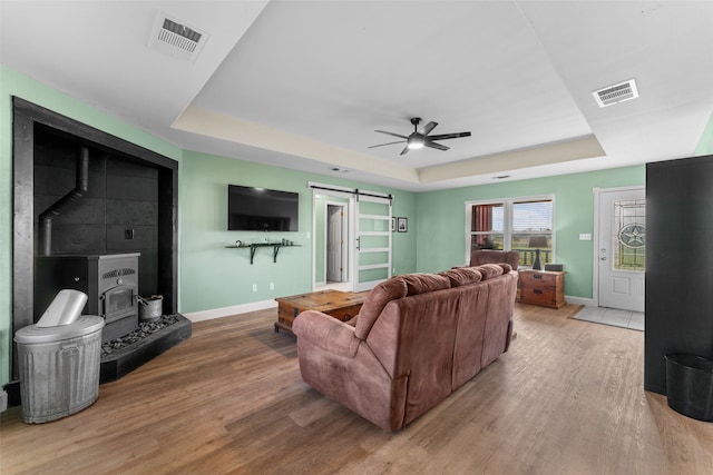 living room with light wood-type flooring, a barn door, a raised ceiling, and ceiling fan