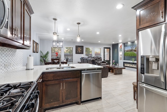 kitchen featuring appliances with stainless steel finishes, backsplash, dark brown cabinets, sink, and decorative light fixtures