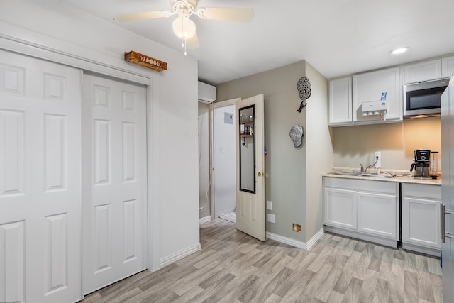 kitchen featuring sink, ceiling fan, a wall mounted AC, light hardwood / wood-style floors, and white cabinetry