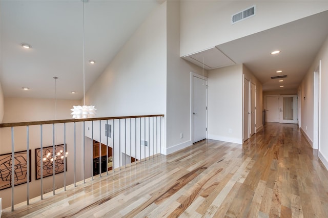 hallway with a high ceiling, an inviting chandelier, and light wood-type flooring