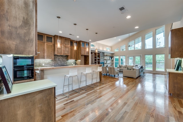 kitchen with pendant lighting, light hardwood / wood-style flooring, backsplash, high vaulted ceiling, and a kitchen bar