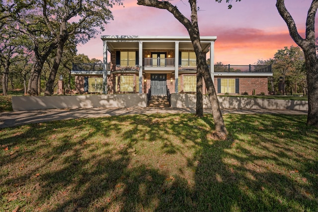 back house at dusk featuring a balcony and a yard