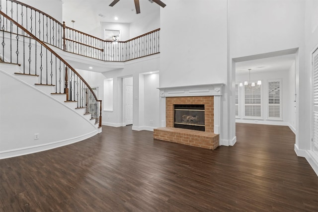 unfurnished living room featuring a fireplace, a high ceiling, ceiling fan with notable chandelier, and dark wood-type flooring