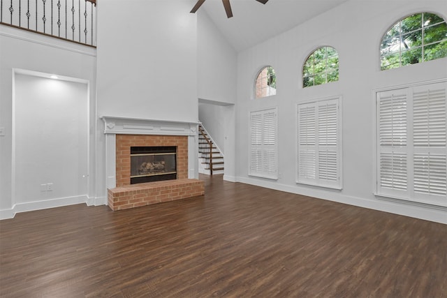 unfurnished living room featuring ceiling fan, dark hardwood / wood-style flooring, high vaulted ceiling, and a brick fireplace