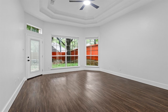 unfurnished room with a raised ceiling, plenty of natural light, ceiling fan, and dark hardwood / wood-style flooring