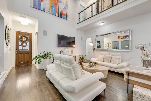 living room with a towering ceiling and dark wood-type flooring