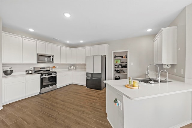 kitchen featuring sink, kitchen peninsula, hardwood / wood-style floors, white cabinets, and appliances with stainless steel finishes