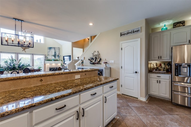 kitchen with white cabinets, stainless steel fridge, decorative light fixtures, and dark stone counters