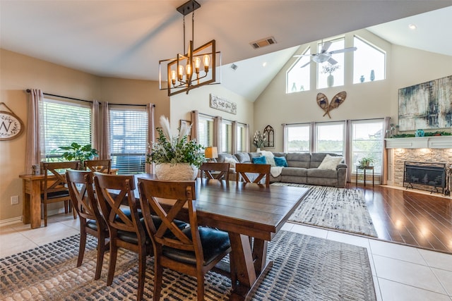 dining area with a fireplace, light hardwood / wood-style flooring, high vaulted ceiling, and ceiling fan with notable chandelier