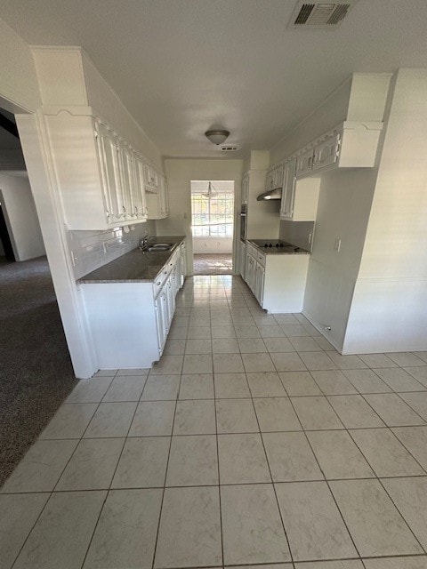 kitchen with light tile patterned flooring, cooktop, white cabinetry, and sink