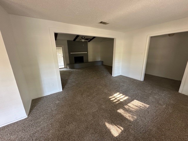 unfurnished living room with dark colored carpet, a textured ceiling, a fireplace, and ceiling fan