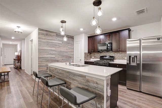 kitchen with a kitchen bar, black appliances, decorative light fixtures, light hardwood / wood-style flooring, and a center island with sink