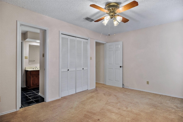 unfurnished bedroom with light carpet, a textured ceiling, ensuite bath, and ceiling fan