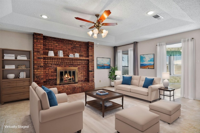 living room featuring ceiling fan, a raised ceiling, a textured ceiling, and a brick fireplace