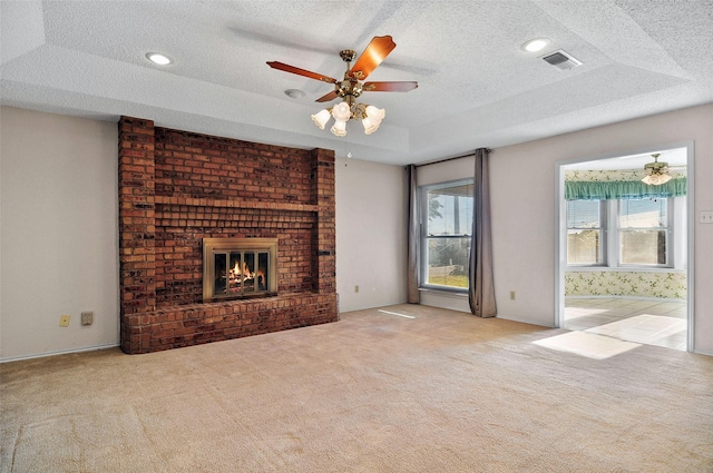 unfurnished living room with a tray ceiling, light carpet, and a brick fireplace