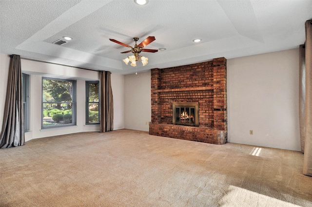 unfurnished living room featuring a fireplace, a textured ceiling, light colored carpet, and a raised ceiling