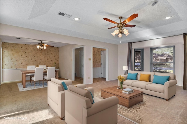 living room featuring ceiling fan, a raised ceiling, a textured ceiling, and light carpet