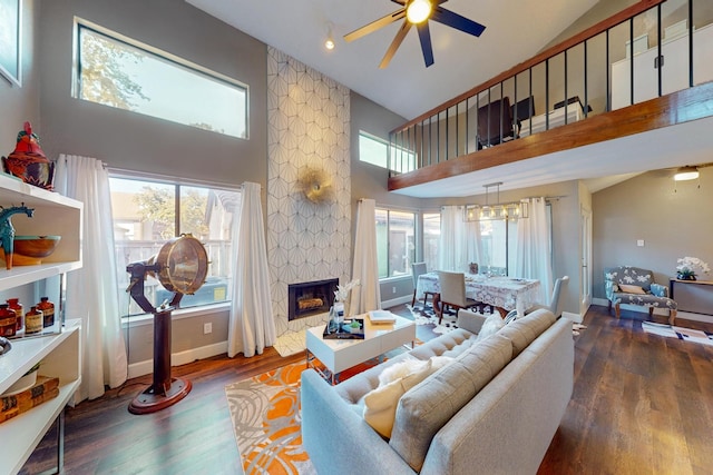 living room featuring a stone fireplace, ceiling fan with notable chandelier, high vaulted ceiling, and dark hardwood / wood-style floors