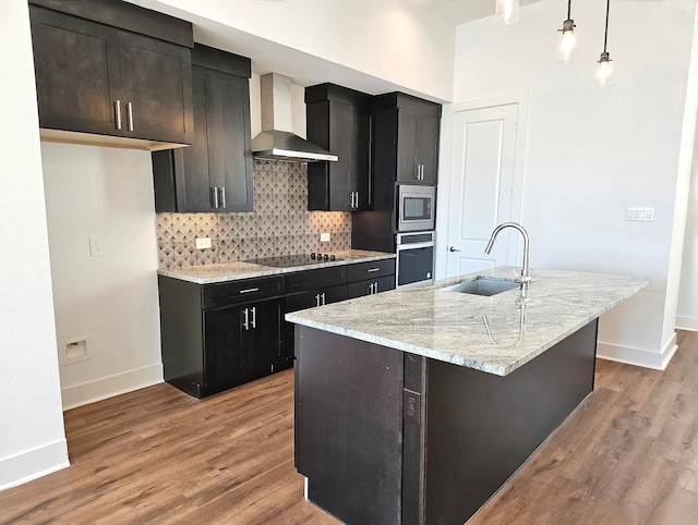 kitchen with sink, wall chimney range hood, pendant lighting, a center island with sink, and appliances with stainless steel finishes