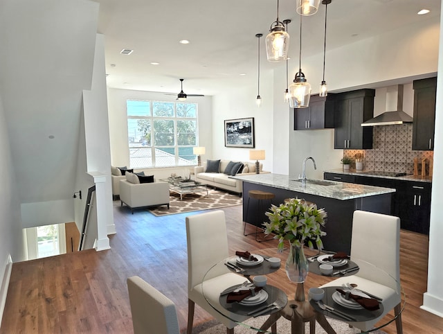 kitchen with light stone countertops, sink, wall chimney range hood, hardwood / wood-style flooring, and an island with sink