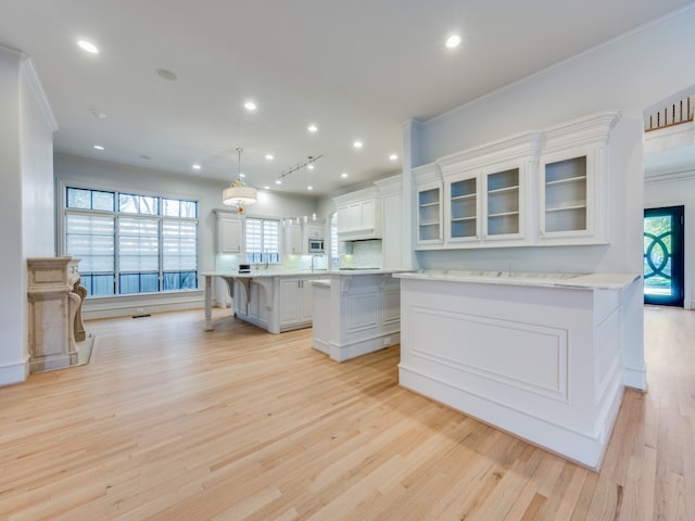 kitchen with pendant lighting, white cabinetry, light hardwood / wood-style floors, a kitchen island, and a breakfast bar area