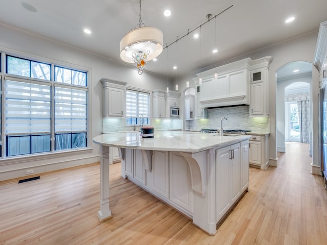 kitchen with white cabinets, hanging light fixtures, a healthy amount of sunlight, and an island with sink