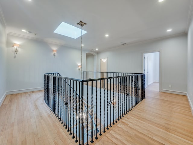 hallway with light wood-type flooring, a skylight, and ornamental molding