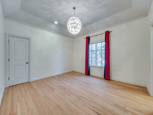 empty room with a raised ceiling, light hardwood / wood-style flooring, an inviting chandelier, and ornamental molding