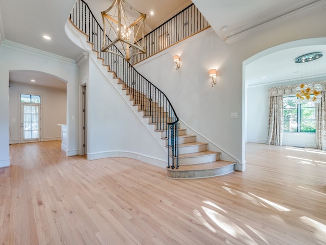 stairway featuring a chandelier, wood-type flooring, plenty of natural light, and crown molding