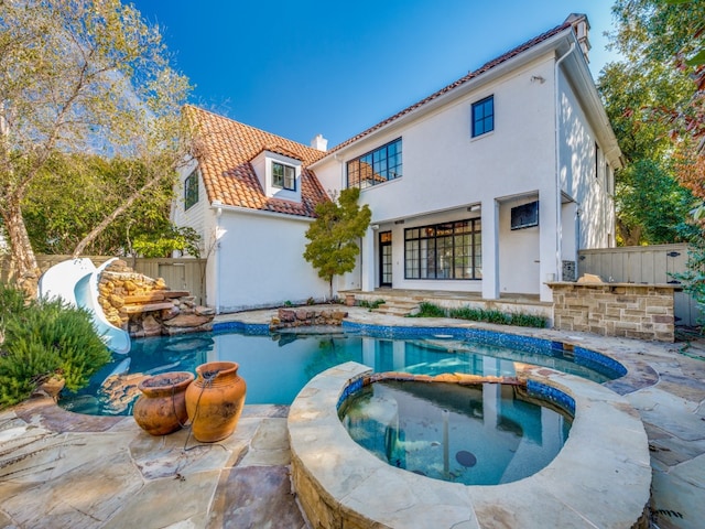 rear view of house featuring a pool with hot tub