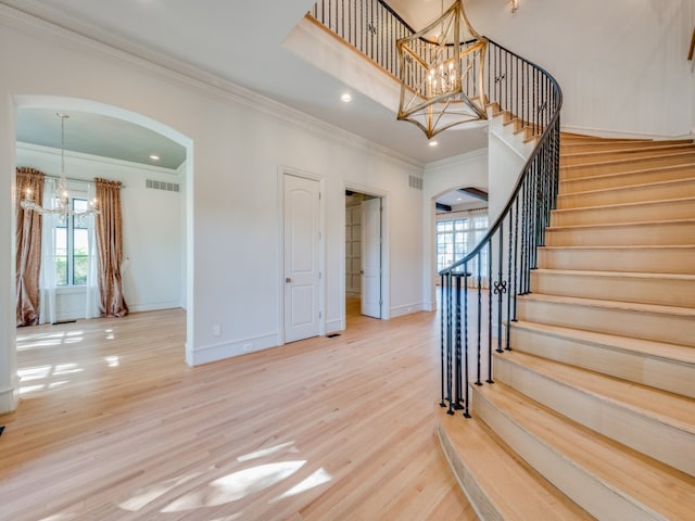 stairway with crown molding, hardwood / wood-style floors, and an inviting chandelier