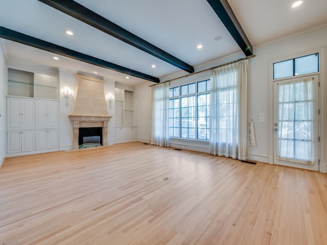 unfurnished living room featuring beam ceiling, a large fireplace, light hardwood / wood-style floors, and crown molding