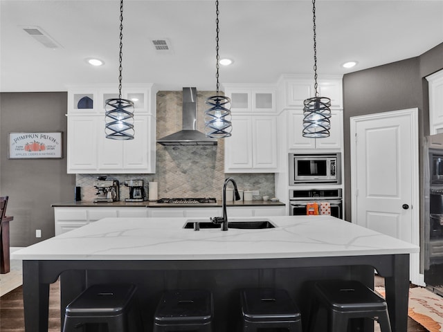 kitchen featuring a kitchen breakfast bar, stainless steel appliances, decorative light fixtures, and wall chimney range hood