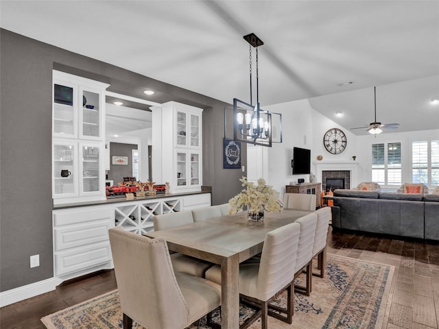 dining area featuring ceiling fan with notable chandelier, lofted ceiling, dark wood-type flooring, and a tile fireplace