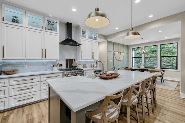 kitchen with white cabinets, wall chimney exhaust hood, a kitchen island with sink, and decorative light fixtures