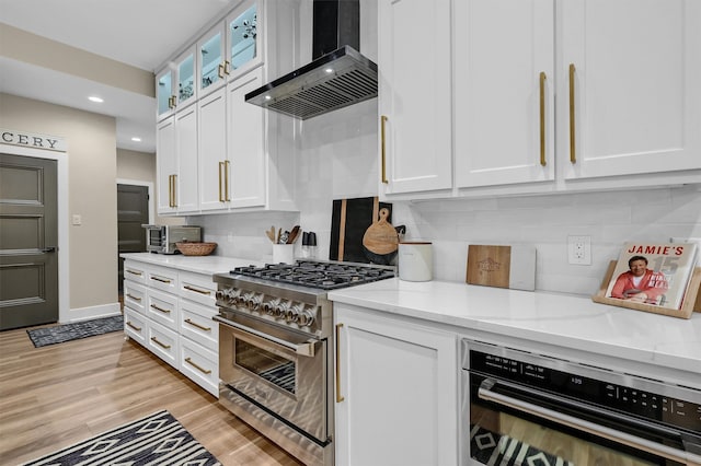 kitchen with light hardwood / wood-style flooring, wall chimney exhaust hood, high end stove, tasteful backsplash, and white cabinetry