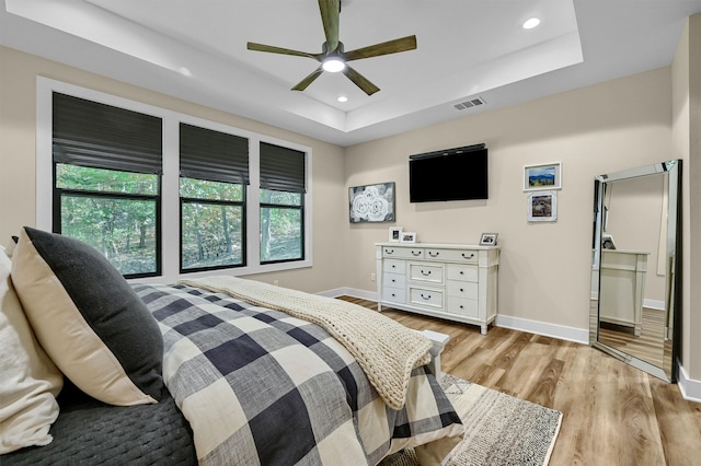 bedroom with ceiling fan, a raised ceiling, and light wood-type flooring