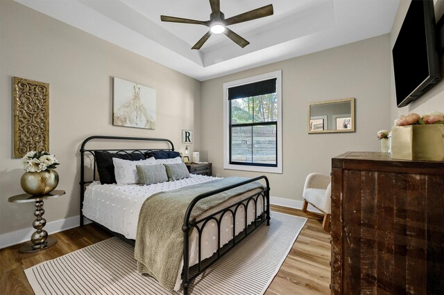 bedroom featuring hardwood / wood-style floors, a raised ceiling, and ceiling fan