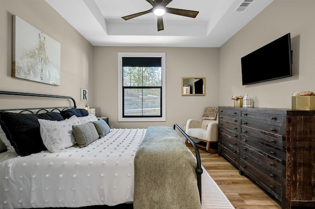 bedroom with ceiling fan, a raised ceiling, and light hardwood / wood-style flooring