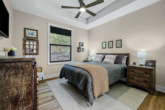 bedroom featuring a raised ceiling, ceiling fan, and light wood-type flooring