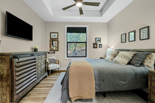 bedroom featuring light hardwood / wood-style floors, ceiling fan, and a tray ceiling