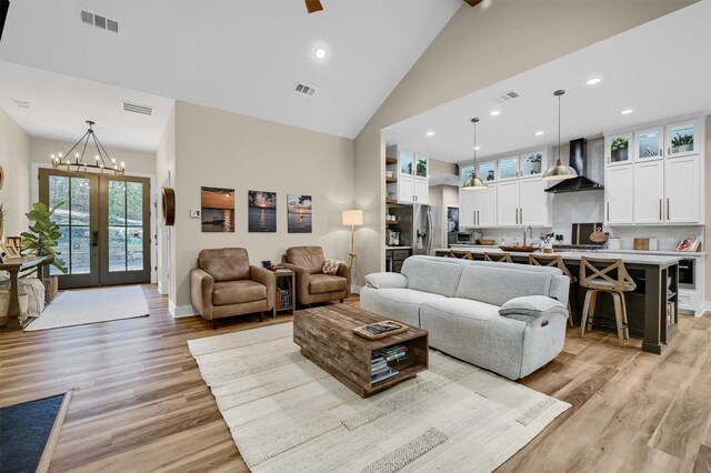 living room with a chandelier, french doors, light hardwood / wood-style floors, and high vaulted ceiling