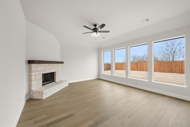 unfurnished living room with ceiling fan, wood-type flooring, a stone fireplace, and vaulted ceiling