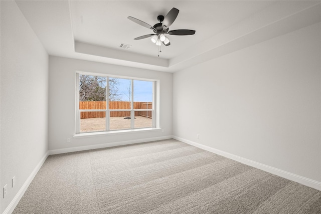 carpeted empty room featuring ceiling fan and a raised ceiling