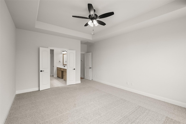 unfurnished bedroom featuring light carpet, connected bathroom, ceiling fan, and a raised ceiling