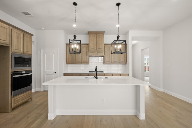 kitchen featuring stainless steel oven, built in microwave, light wood-type flooring, an island with sink, and backsplash