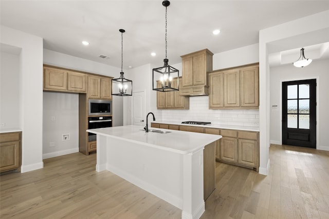 kitchen featuring stainless steel microwave, black gas cooktop, backsplash, wall oven, and a center island with sink