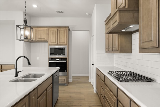 kitchen featuring appliances with stainless steel finishes, custom range hood, sink, decorative light fixtures, and light wood-type flooring