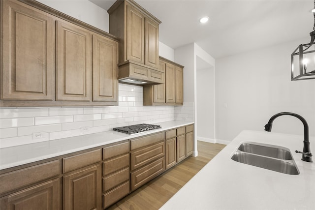 kitchen with stainless steel gas cooktop, decorative backsplash, sink, decorative light fixtures, and light wood-type flooring